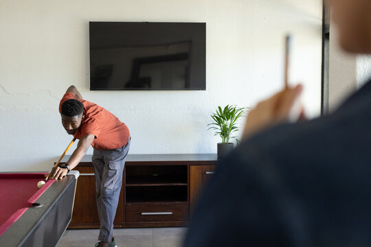 African American man leaning over red-felt pool table aiming cue at white ball in game room