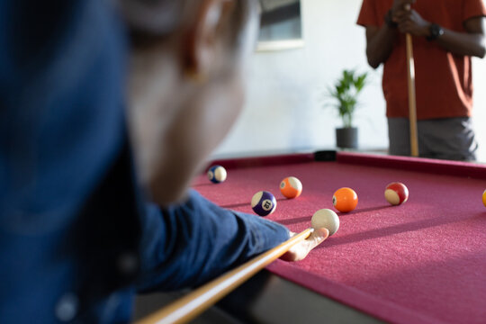 Couple playing pool in recreation room, man lining up shot on burgundy table with numbered balls