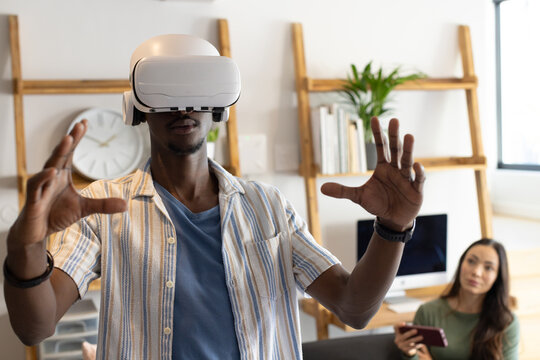 Diverse coworkers testing VR headset in home office, man reaching in striped shirt, woman watching