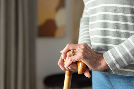 Senior female resting hands on curved wooden cane wearing striped sweater in living room