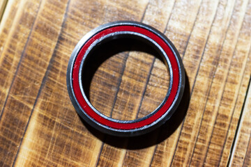 Close-up of a high-quality bicycle headset cartridge bearing with red seals, resting on a textured wooden background