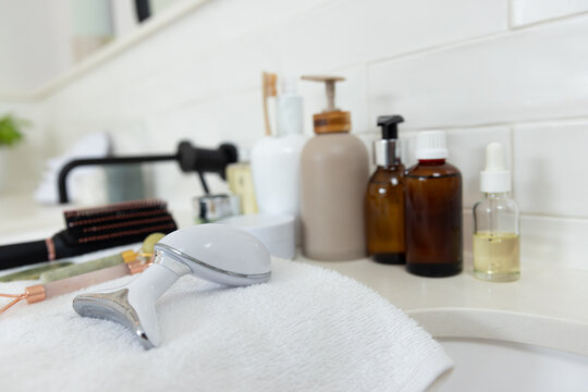 White handheld facial massager is resting on folded white towel on vanity with amber dropper nearby