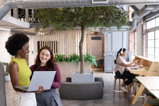 Diverse female team reviewing laptop while colleague typing with headphones and coffee, copy space