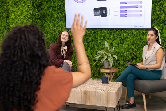 Three women leading panel discussion in modern meeting lounge, holding microphones and tablet