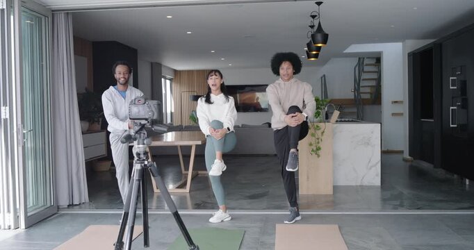 Diverse friends arranging mats as tripod camera rolling and doing knee holds at home for filming