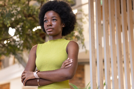 African woman standing with arms crossed in atrium, wearing lime-green top, smartwatch