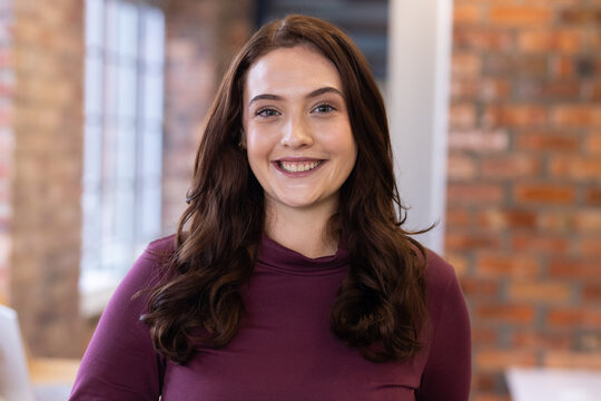 Female smiling and facing camera while wearing maroon long-sleeve top at coworking desk with laptop