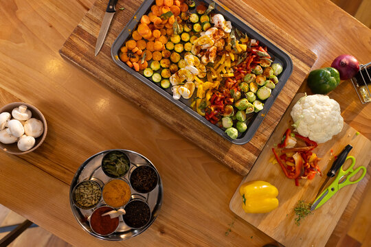 Rectangular metal baking tray is holding sliced vegetables and eggs on wooden table with spice box