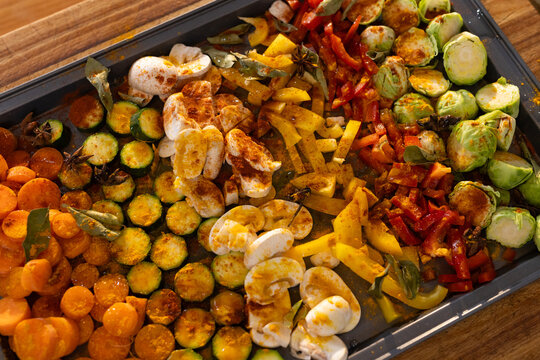 Metal baking tray is holding seasoned vegetable rows on wooden countertop, lit by warm light