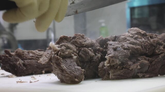 노란 장갑을 낀 손으로 도마 위에서 잘 삶아진 고기를 손질하는 조리 과정 클로즈업 뷰