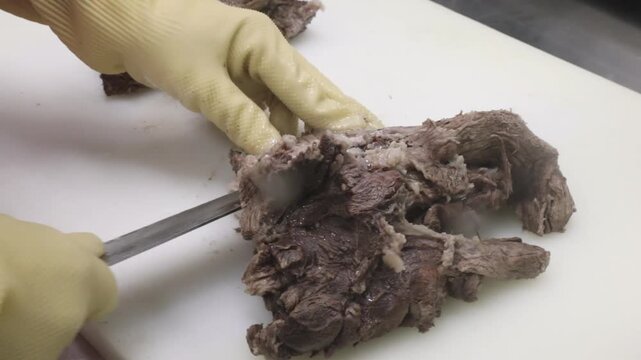 노란 장갑을 낀 손으로 도마 위에서 잘 삶아진 고기를 손질하는 조리 과정 클로즈업 뷰