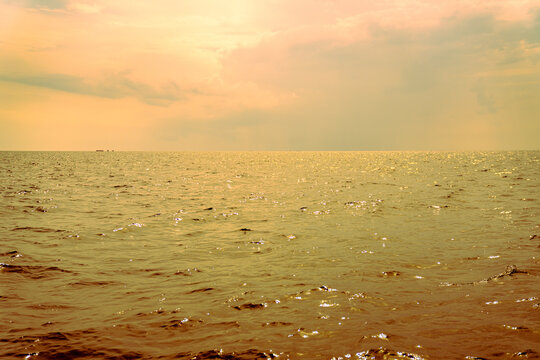 Beautiful golden sunset over the calm sea waves. The sun shines through the clouds, reflecting on the ocean surface. Peaceful nautical landscape with a warm orange and yellow vintage color palette.