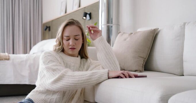 Adult female wearing chunky sweater, sitting by sofa, reading bad news on maroon phone