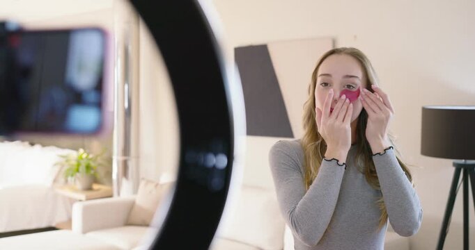 Adult female reacting to ringlight, wiping undereye with pad, applying pink patches