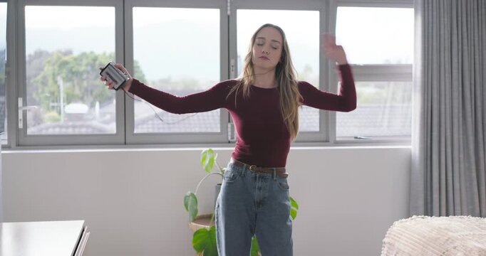 Adult woman raising arms, dancing to music, holding corded device at bedroom window