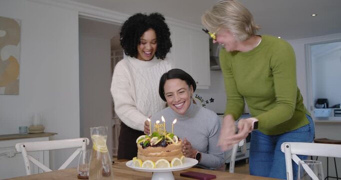 Diverse female friends entering kitchen surprising scrolling woman, with cake and sash for birthday