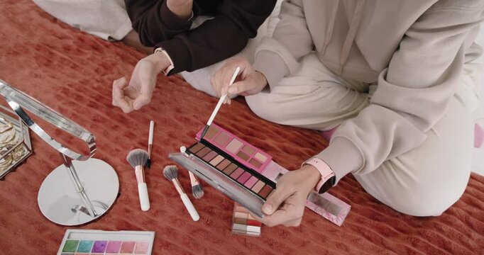 Opening pink palette on quilt, friends are dipping brushes, testing shades on wrists to match tones