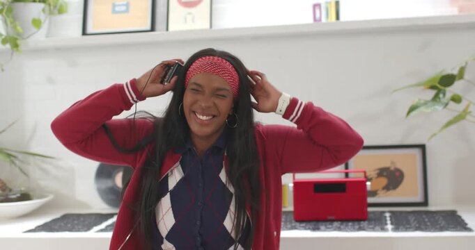 African American woman putting wired headset listening to player checking watch dancing in kitchen