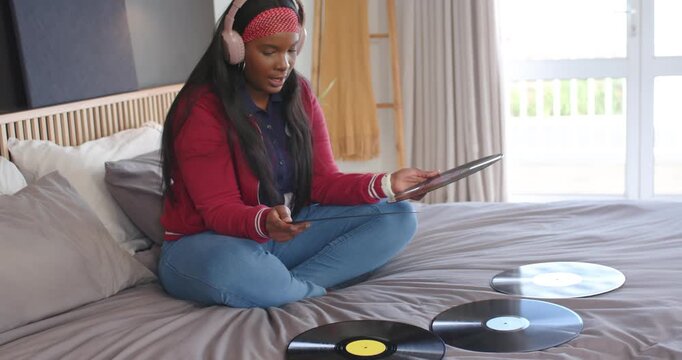 African American woman on bed picking records, putting on pink headphones, choosing vinyl to play