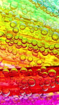 Gas bubbles move through water in a vertical macro video. Transparent gas bubbles drift over bright abstract color surfaces.