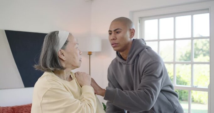 Senior Chinese woman and male aide holding wrist guiding arm across chest by window for mobility