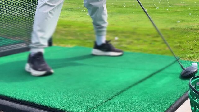 A golfer standing on a green driving range mat, addressing a ball resting on an automated rubber tee with a driver club.