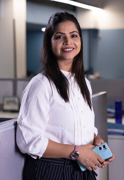 Portrait of a indian young working businesswoman wearing corporate white shirt while looking at camera in a modern office.