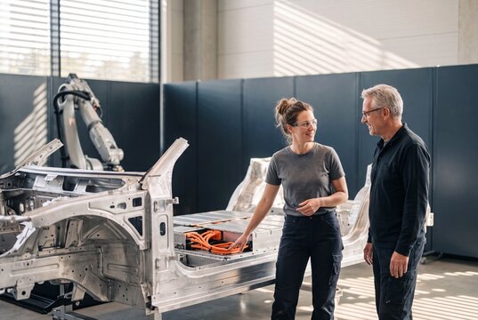 Automotive engineers discussing electric vehicle chassis and battery pack assembly in a high-tech manufacturing plant
