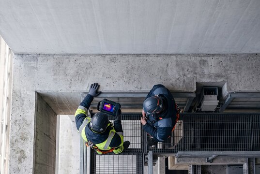Top view of two engineers using a thermal imaging camera to inspect a concrete building structure on an industrial site