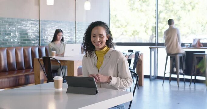 Mid-adult African American woman accepting tablet call, gesturing, smiling, discussing work at cafe