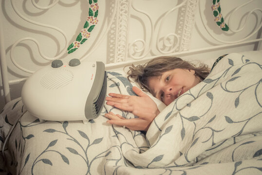 Woman warming hands in front of a portable electric heater in bed