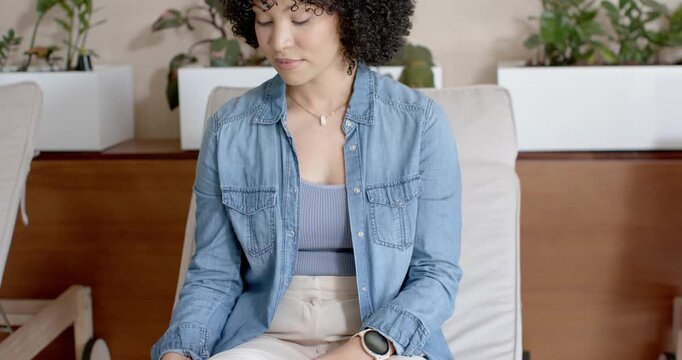 African-American woman sitting on lounge chair after shifting grabbing smartphone tapping scrolling