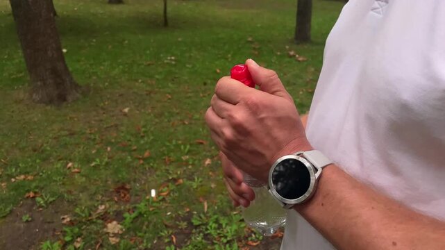 Man using a red spray bottle while outdoors in a park, active lifestyle and personal care, healthy routine, leisure activity.