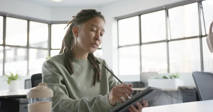 Nonbinary designer starting sketch sitting at desk by window, holding stylus refining art on tablet