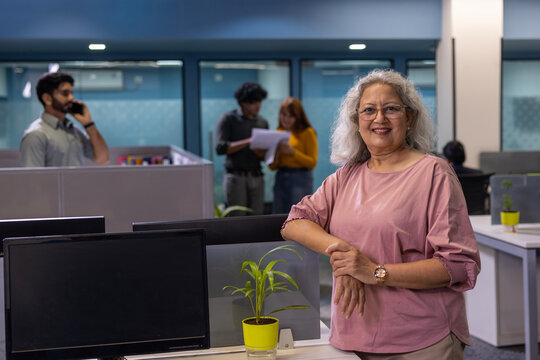 Indian senior aged business woman standing at workplace. Smiling older senior businesswoman, 65s white-haired lady Business owner looking at camera in office, portrait.