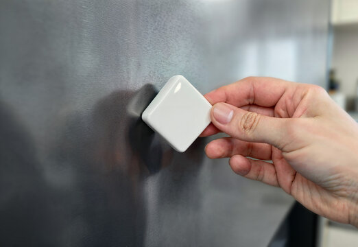 Blank rhombus souvenir magnet held by hand on refrigerator, ai generated. Magnets attached to steel fridge surface by arm. Home decor, clean design for memory photo or vacation pin concept.