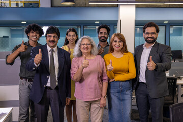 Fototapeta premium Happy diverse professional team standing together in a modern office and giving thumbs up to the camera. Smiling coworkers celebrating teamwork, positive workplace culture, collaboration, confidence, 