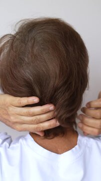 Back view of mature woman touching hair and demonstrating gray roots and natural graying at the crown on a light background