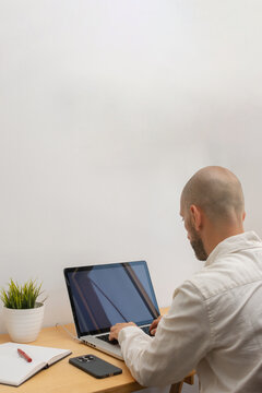 Vertical rear view of man typing on laptop at wooden desk
