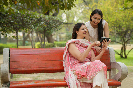 Indian happy mother having fun caring, hugging, enjoyment and  bonding loving with her daughter. Two indian woman sitting and enjoying at park. 