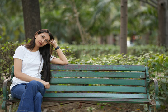 Indian young girl feeling guilty, sad, depressed, disappointed, trouble, loss, stressful, anxiety, confused and discomfort while sitting on bench at outdoor park.