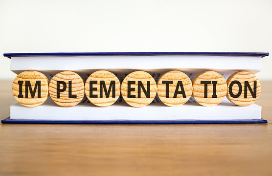 Implementation word symbol. Concept word Implementation on beautiful wooden circles in book. Beautiful wooden table white background. Business implementation word concept. Copy space.
