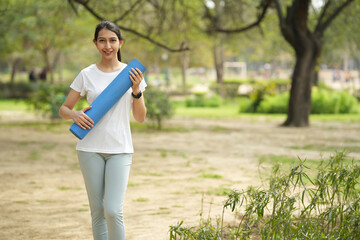 Fototapeta premium Indian young girl holding yoga matt while standing at park