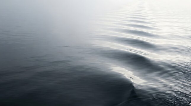 Gentle ocean water surface displays subtle wave patterns with soft light and muted grayscale tones aqueous calm