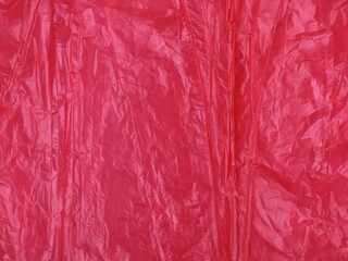 Obraz premium Close up of the texture of bright red wrinkled plastic film. Creased surface, folds, and highlights create a detailed abstract background, perfect for design, packaging concepts, or overlays