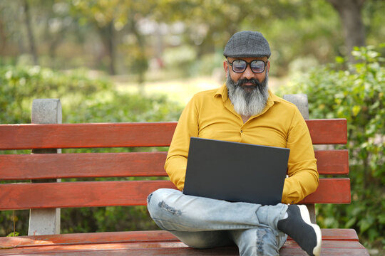 Portrait od cheerful smiling indian senior man working on laptop in garden. Happy Elderly white-haired people smiling carefree, old Bearded male with positive emotion. all good expression.