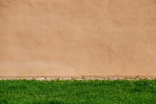 Green grass patch against textured beige wall. Urban scene is simple and minimalistic, highlighting the contrast between the grass and blank brown building wall.