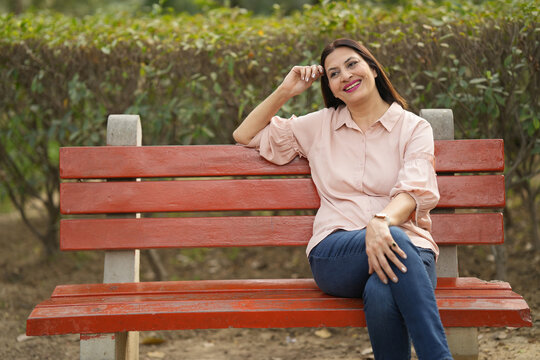 Portrait of happy woman relaxing at park. Indian happy young female spending leisure time at park while sitting on bench.