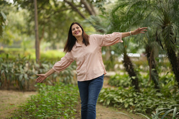 Indian happy woman spread her arms in environment nature like the wings of a bird. Happiness. Freedom. young woman stands with one hand open in a park. Indian active mid aged fun woman in park © Pix4Ads