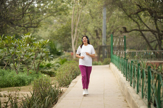 Indian happy woman doing joking running and walking in garden ramp with headphone listening music feeling good